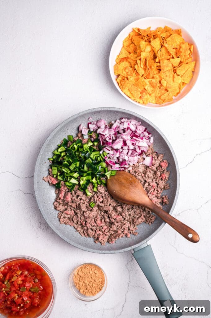 Ground beef cooking in a skillet with red onion and poblano pepper, ready for seasoning.