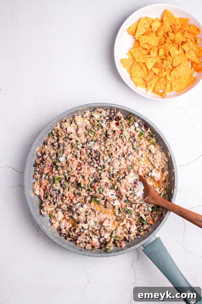 The seasoned ground beef mixture with diced tomatoes, black beans, and sour cream, fully combined in a skillet.