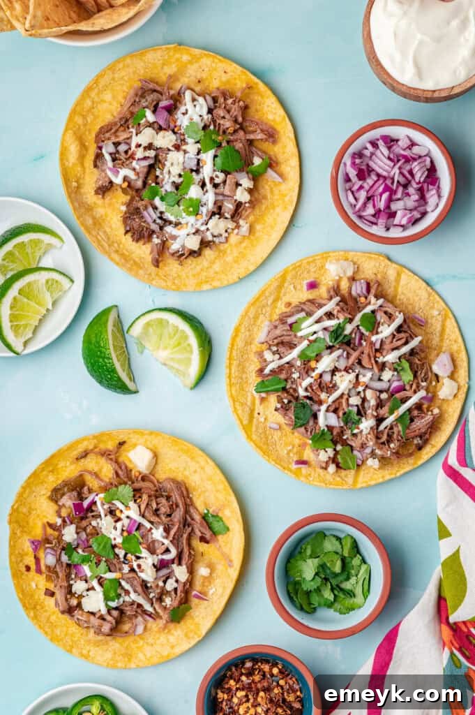 A vibrant platter of assembled Slow Cooker Pulled Pork Tacos, showcasing colorful toppings and fresh ingredients against a blue background.