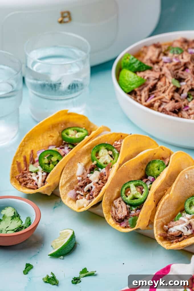 Three perfectly assembled Slow Cooker Pulled Pork Tacos arranged on a rustic wooden board, garnished with fresh cilantro and a squeeze of lime, on a blue background.