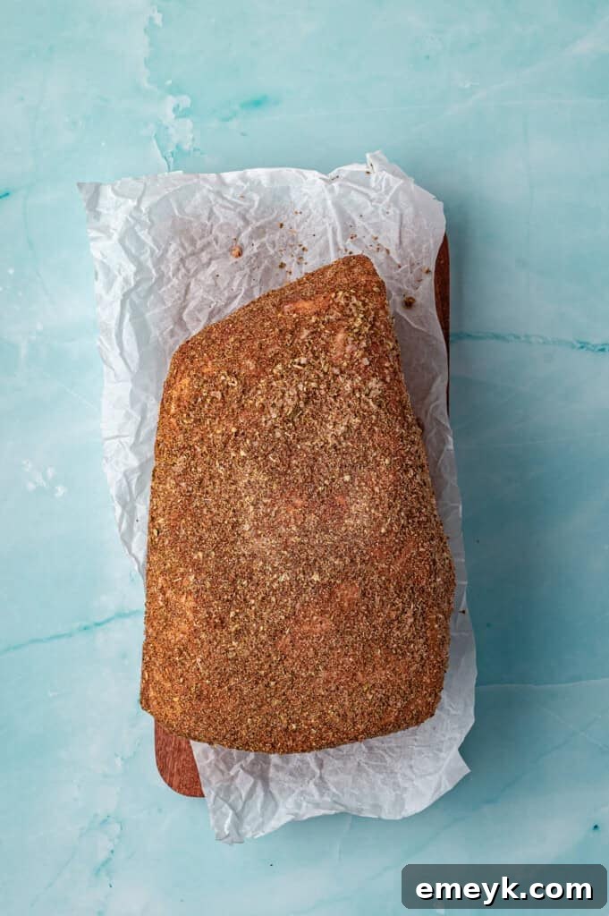 The pork shoulder, generously coated with the spice rub, placed inside a slow cooker ready for the next ingredients to be added around it.