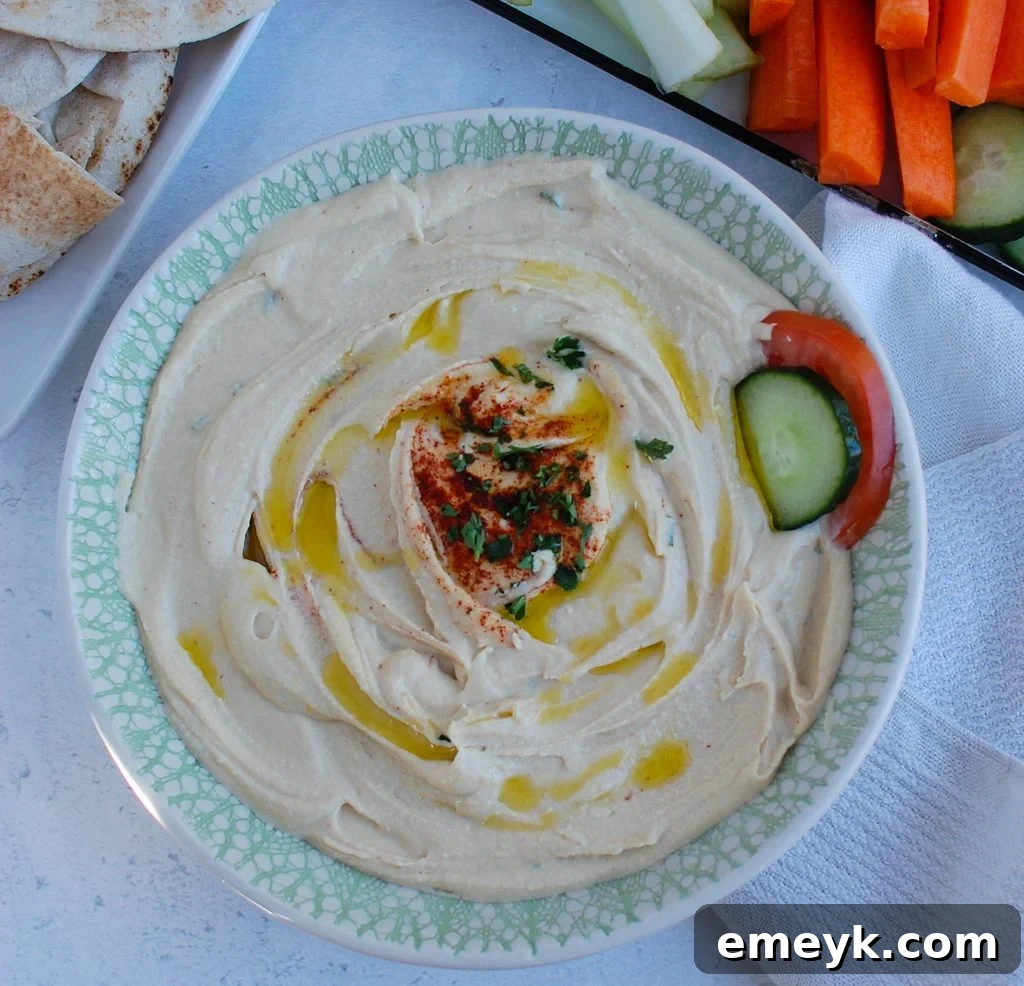 A bowl of creamy Lebanese Hummus on a wooden table, with a red napkin and fresh parsley sprigs as garnish.