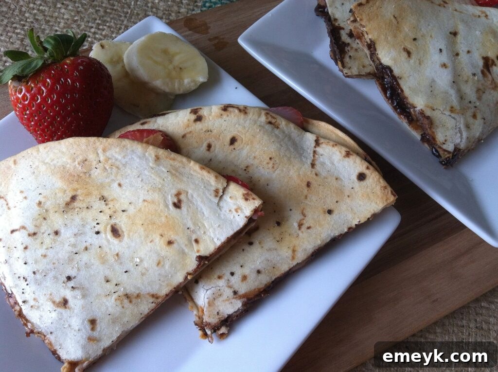 Two dessert quesadilla halves revealing vibrant layers of banana, strawberry, peanut butter, and chocolate chips.