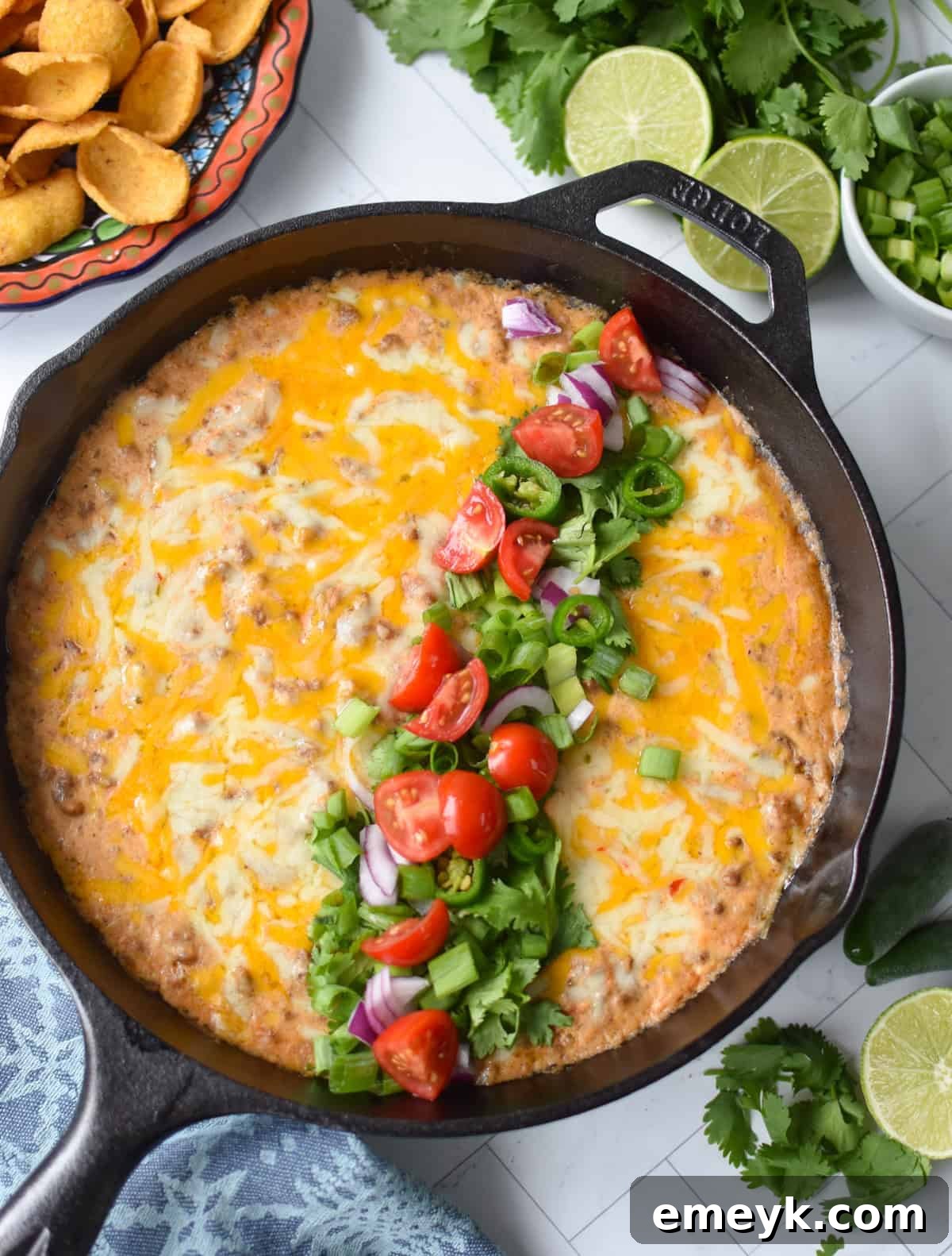 Beefed-Up Cottage Cheese Queso 4 Cottage cheese beef dip baked in a black cast iron skillet and garnished with diced tomatoes, green onion, cilantro and red onions up above with chips on a plate.
