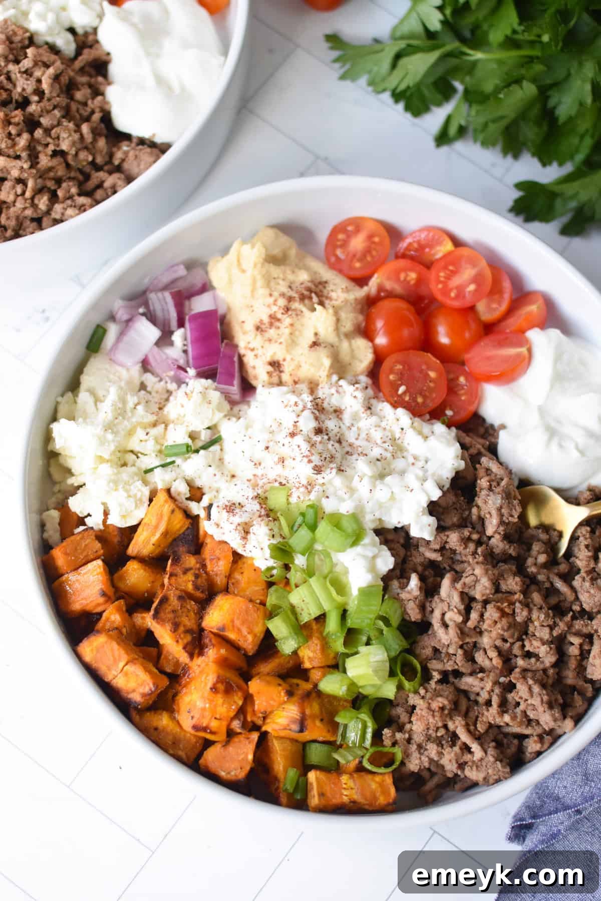 A beautifully arranged Sweet Potato Cottage Cheese Bowl with a golden fork, showcasing roasted sweet potatoes, spiced ground beef, cottage cheese, Greek yogurt, and fresh herbs in a white ceramic bowl.