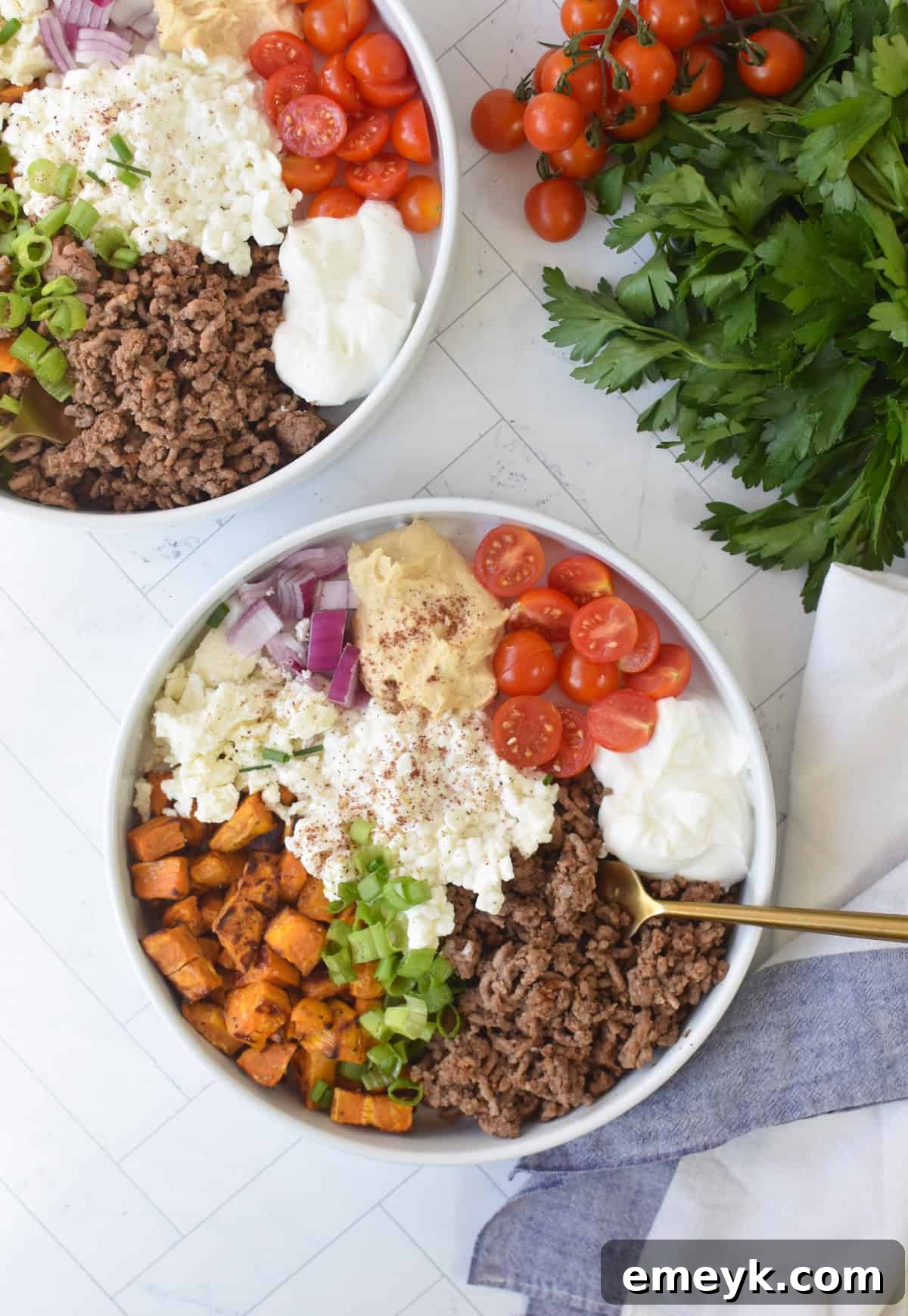 Close-up of a Sweet Potato Cottage Cheese Bowl, showcasing the layers of ingredients: spiced beef, roasted sweet potatoes, cottage cheese, and fresh garnishes, with a napkin and fork beside it.