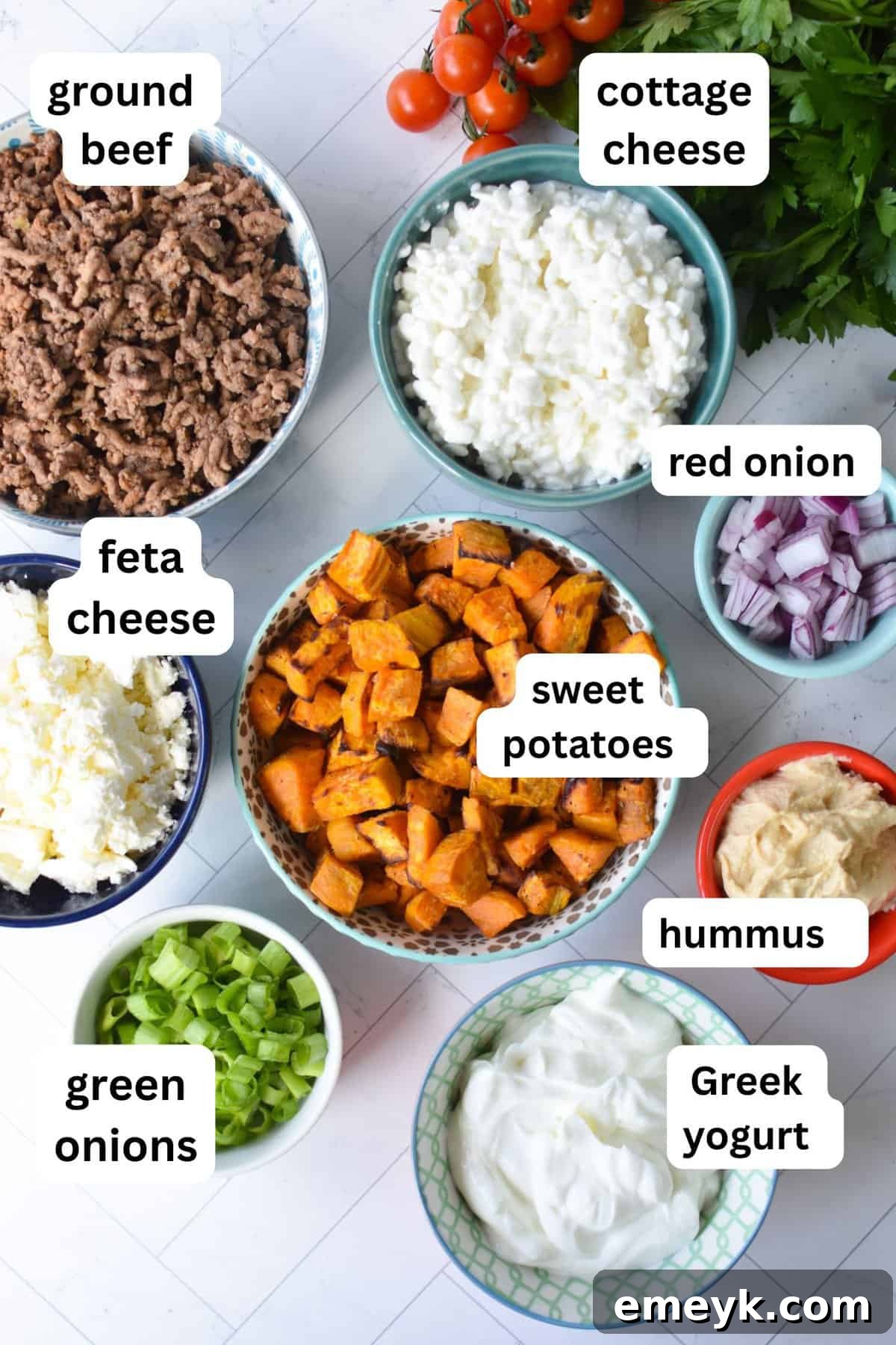 A vibrant flat lay of all the fresh ingredients needed for Sweet Potato Cottage Cheese Bowls, including ground beef, sweet potatoes, various spices, cottage cheese, and Greek yogurt, on a rustic wooden board.