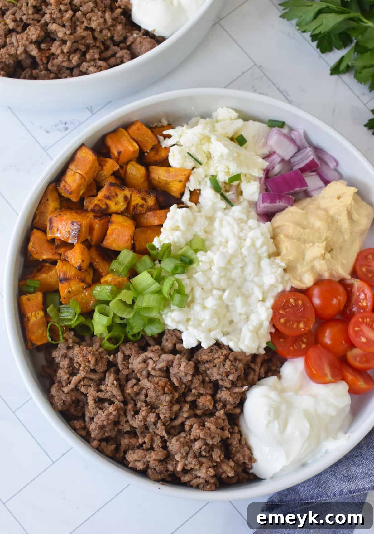 A finished Sweet Potato Cottage Cheese Bowl, generously topped with fresh garnishes like feta, red onion, tomatoes, and parsley, ready to be enjoyed.
