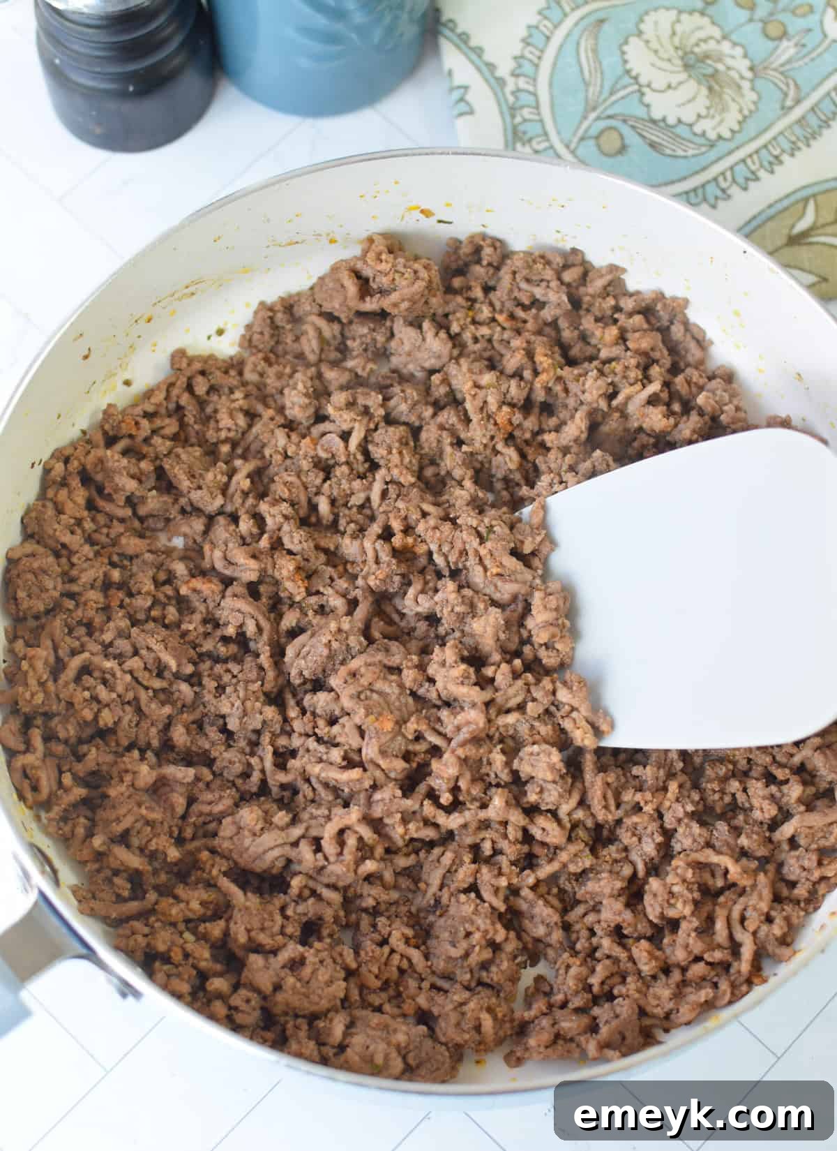 Ground beef being cooked in a large skillet on a stovetop, with onions and spices, as part of the Sweet Potato Cottage Cheese Bowls recipe preparation.