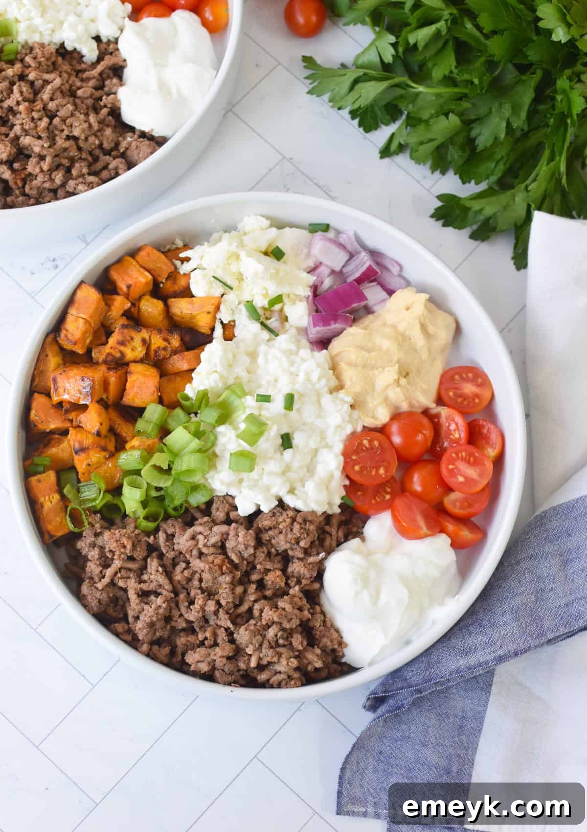 A neatly arranged Sweet Potato Cottage Cheese Bowl, highlighting the fresh, colorful garnishes and fluffy texture of the cottage cheese, set on a dark surface with a white napkin.