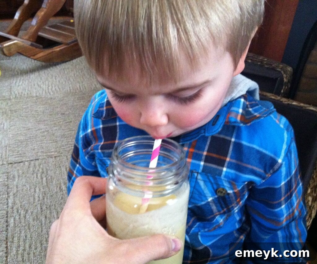 A young child happily enjoying a Mango Banana Oatmeal Breakfast Smoothie, showcasing its kid-friendly appeal