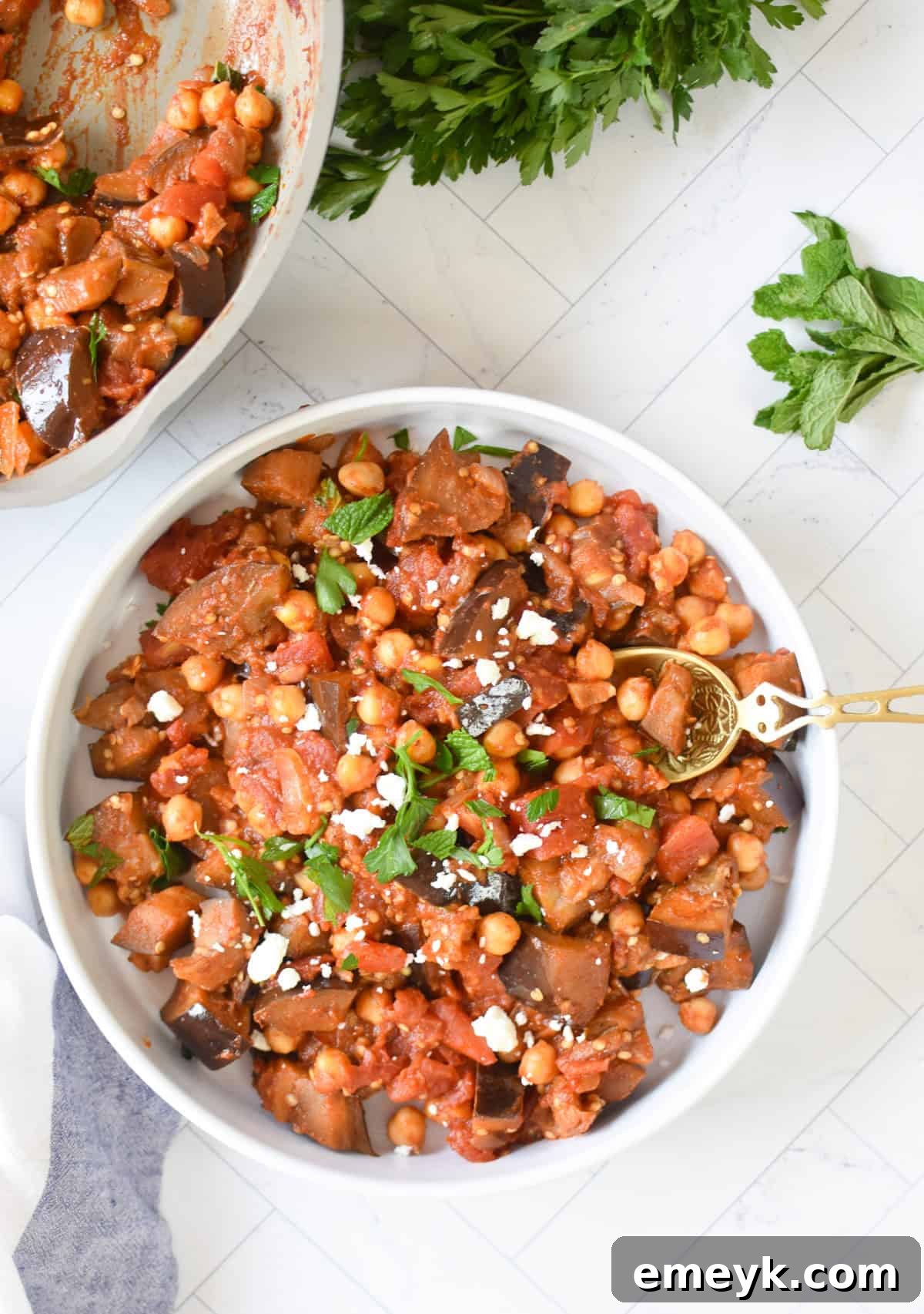 Lebanese Maghmour Hearty Eggplant and Lentil Casserole 7 A serving of Lebanese Moussaka in a white bowl with a gold spoon, garnished with fresh herbs, ready to be enjoyed.