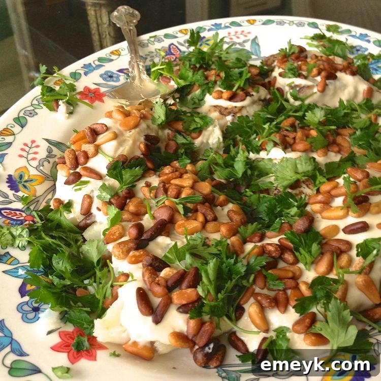 Easy Baked White Fish Recipe on a white plate, garnished with parsley and golden pine nuts, with lemon wedges.