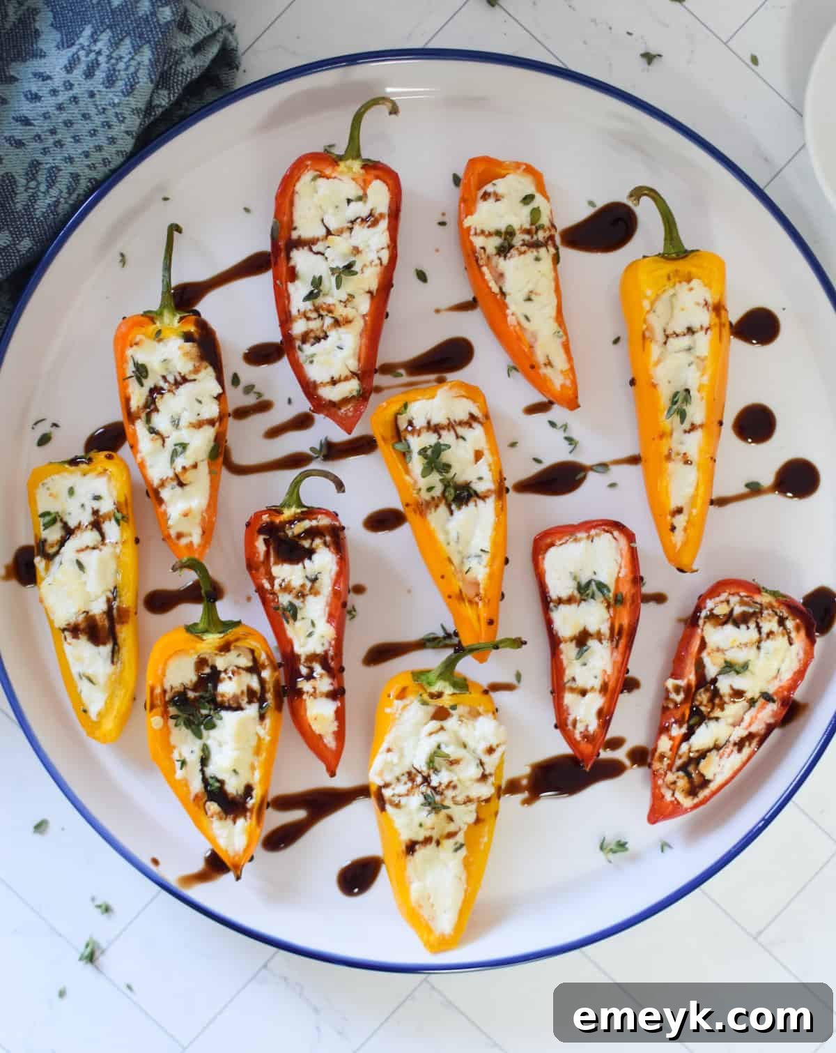 Creamy Goat Cheese-Filled Mini Peppers 2 Vibrant Goat Cheese Stuffed Mini Peppers artfully arranged on a white and blue plate, ready to be served as an appetizer.
