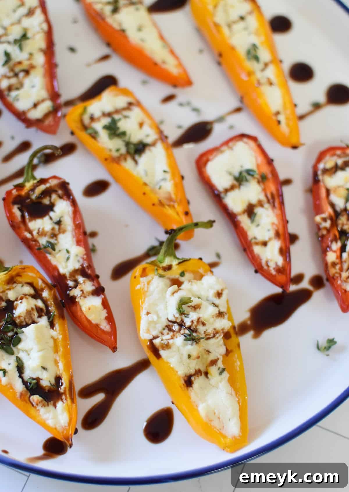Creamy Goat Cheese-Filled Mini Peppers 3 Close-up of baked Goat Cheese Stuffed Mini Peppers on a white and blue plate, highlighting the melted cheese and vibrant pepper colors.