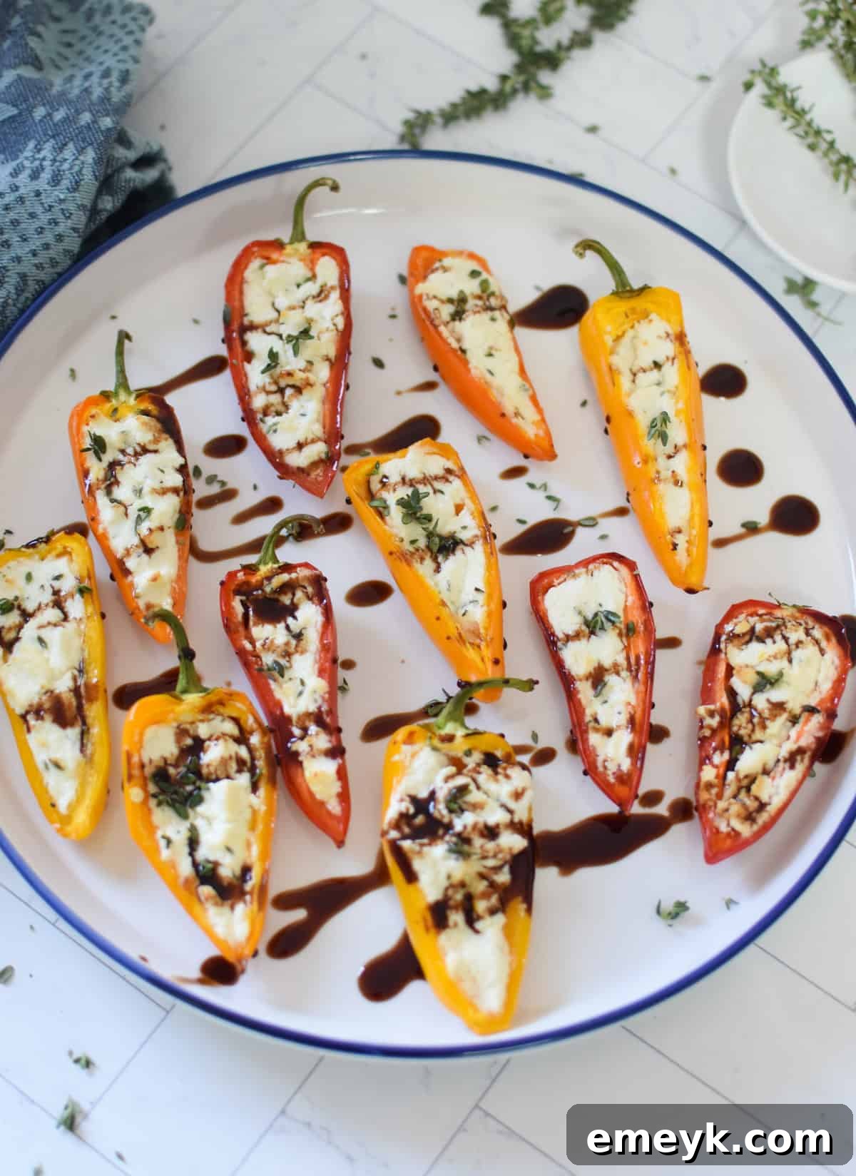 Creamy Goat Cheese-Filled Mini Peppers 8 Baked Goat Cheese Stuffed Mini Peppers drizzled with balsamic glaze, served on a white plate with fresh thyme.