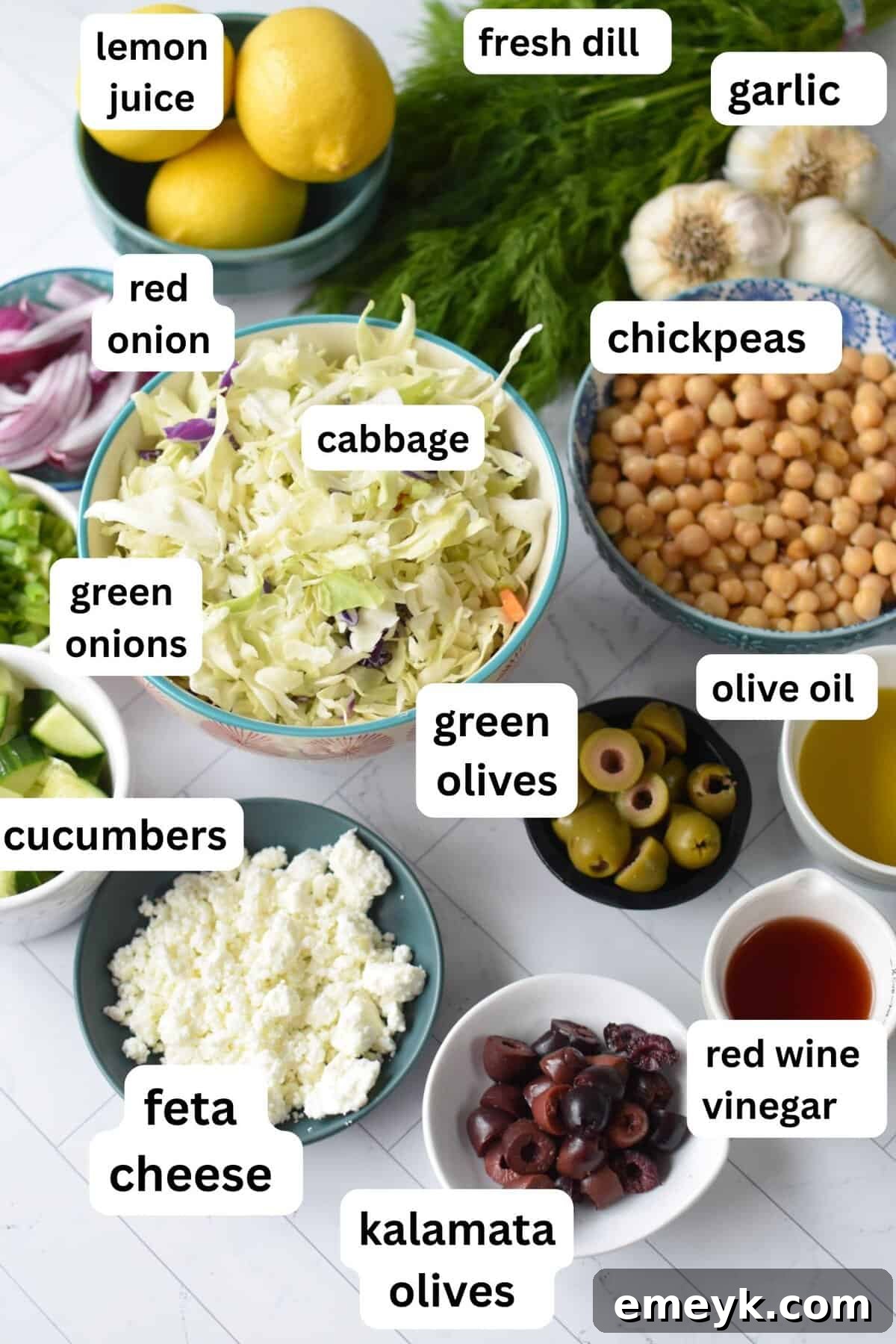 Assortment of fresh ingredients for Greek Cabbage Salad including shredded cabbage, chickpeas, olives, and herbs.