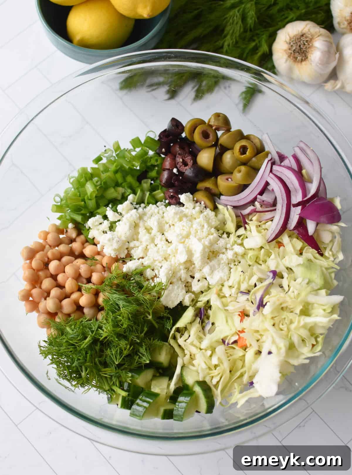 All prepared Greek Cabbage Salad ingredients in a large clear mixing bowl, ready for dressing.