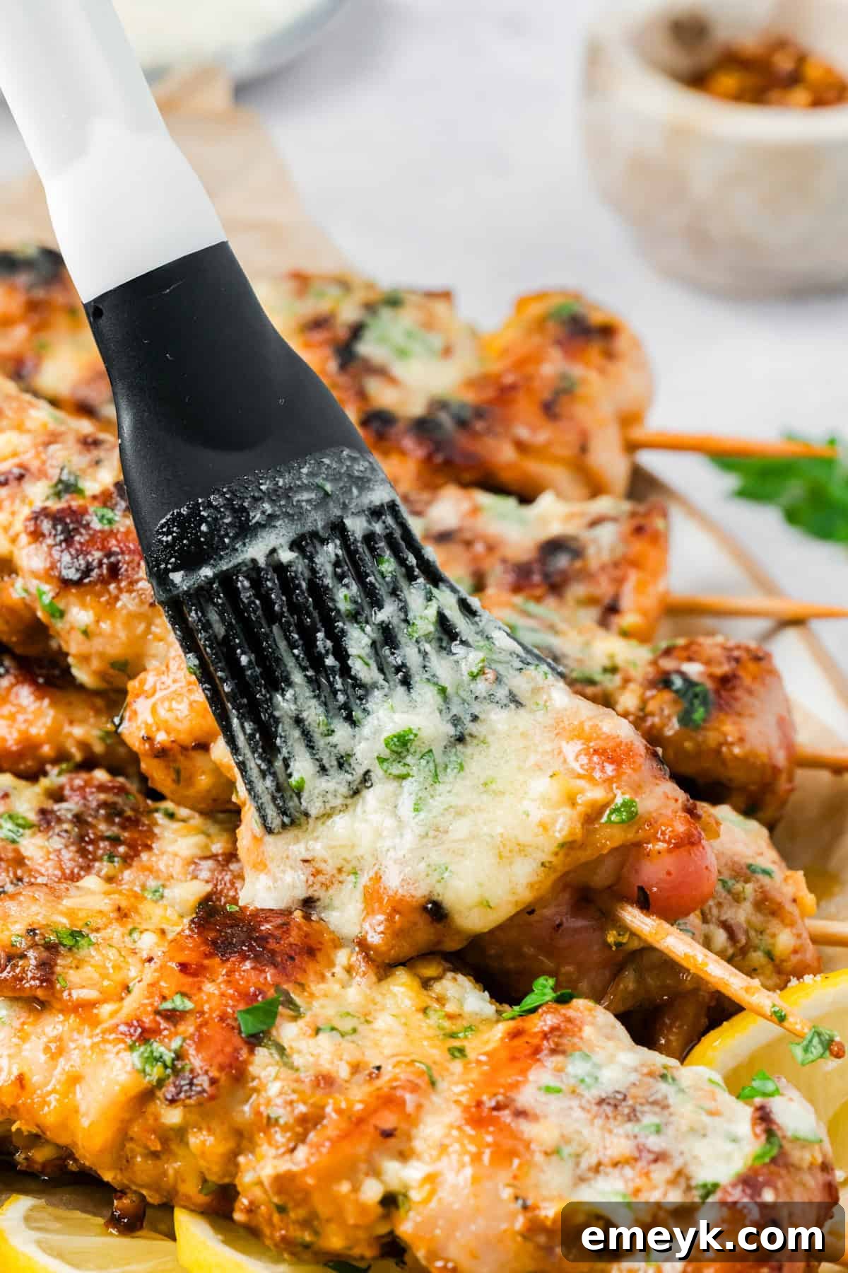 Grilled chicken skewers being brushed with garlic Parmesan butter sauce.