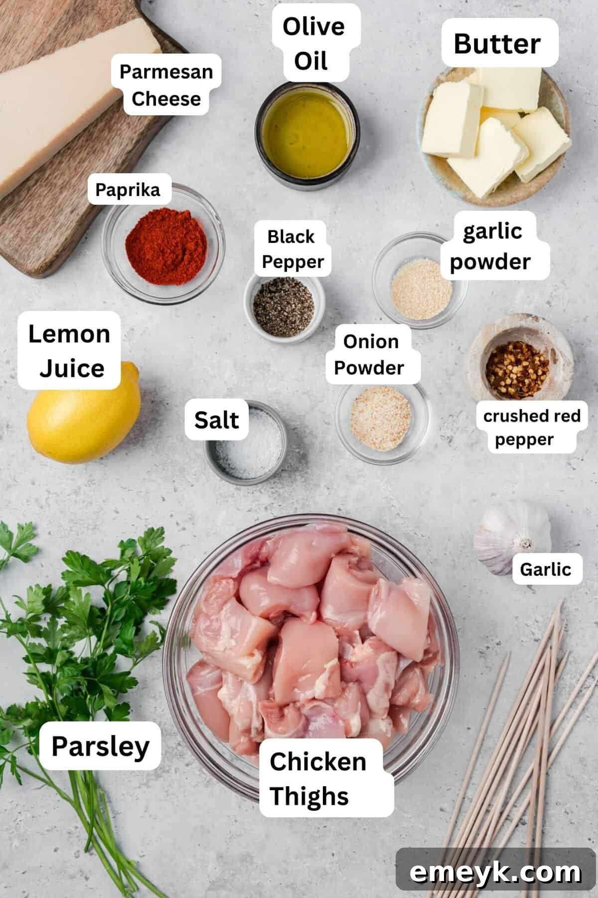 Raw chicken thighs, spices, butter, garlic, and Parmesan cheese, laid out as ingredients for chicken skewers.