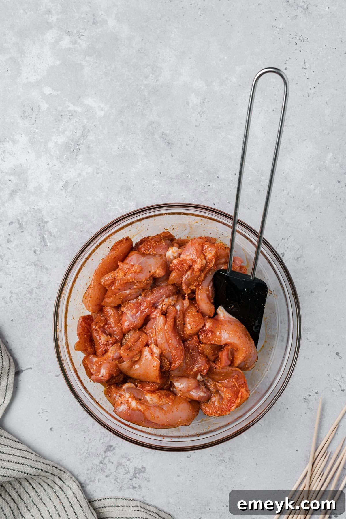 Chicken pieces marinating in a bowl with olive oil and spices for garlic Parmesan skewers.