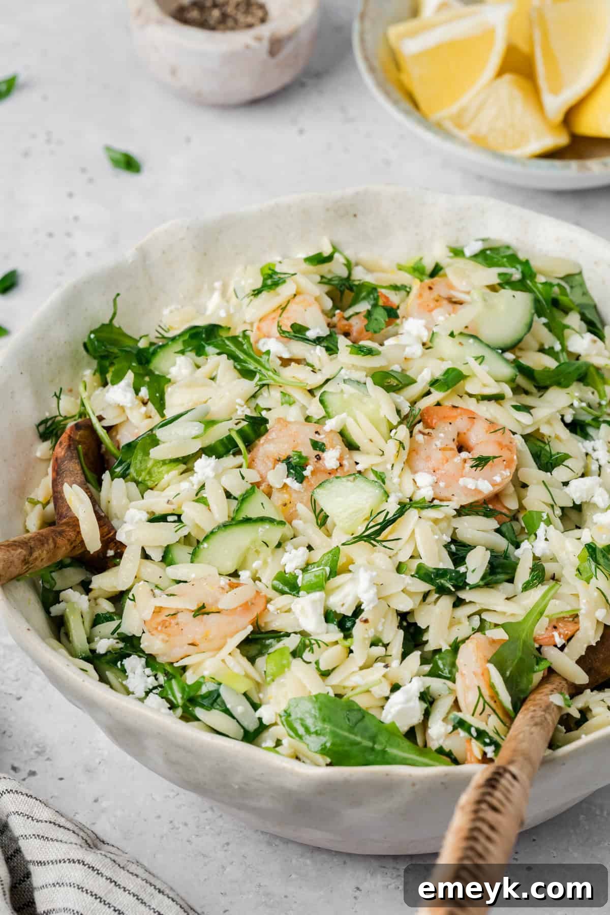 Shrimp Orzo Pasta Salad in a white bowl with a wooden spoon