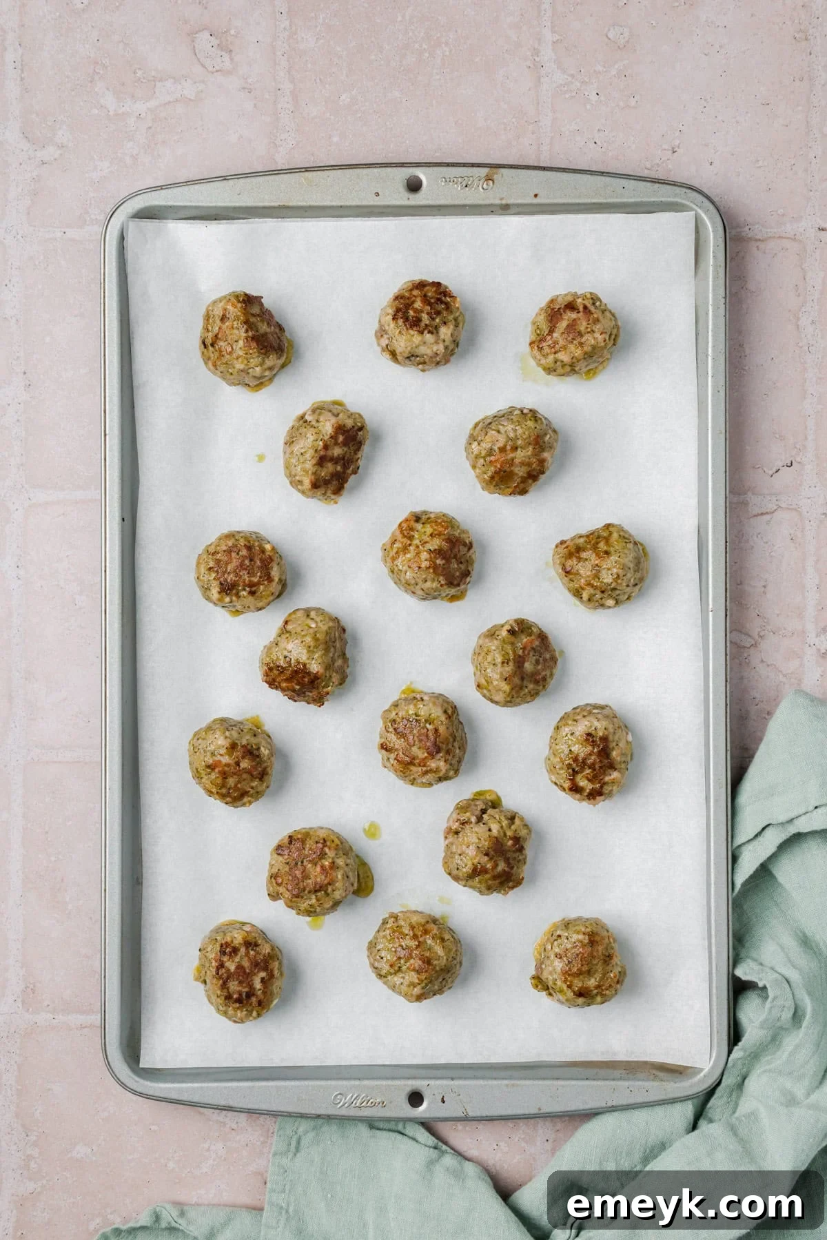 Turkey meatballs with pesto on baking sheet, ready for oven.