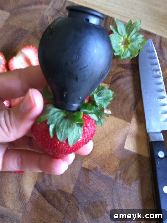 Close-up of a hand using an OXO strawberry huller to remove the stem from a fresh strawberry.