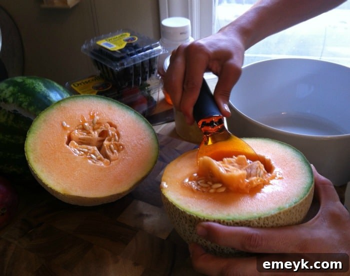 A fresh cantaloupe, halved and expertly deseeded with a fruit scoop, ready for dicing.