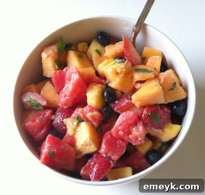 A large, vibrant bowl of fresh fruit salad, glistening with the Yogurt Honey Lemon Dressing and topped with mint.