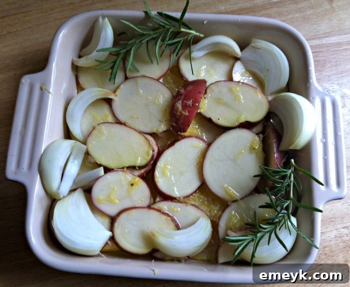 Raw chicken pieces and red potatoes being prepped on a baking sheet with lemon slices and rosemary before roasting