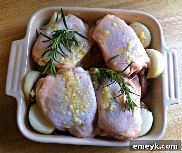 Raw chicken and red potatoes seasoned with lemon, rosemary, and garlic, arranged on a baking sheet with lemon slices, ready for the oven