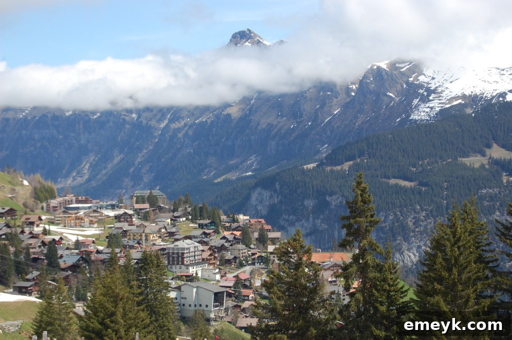 A winding hiking trail through vibrant green fields with the village of Mürren in the distance