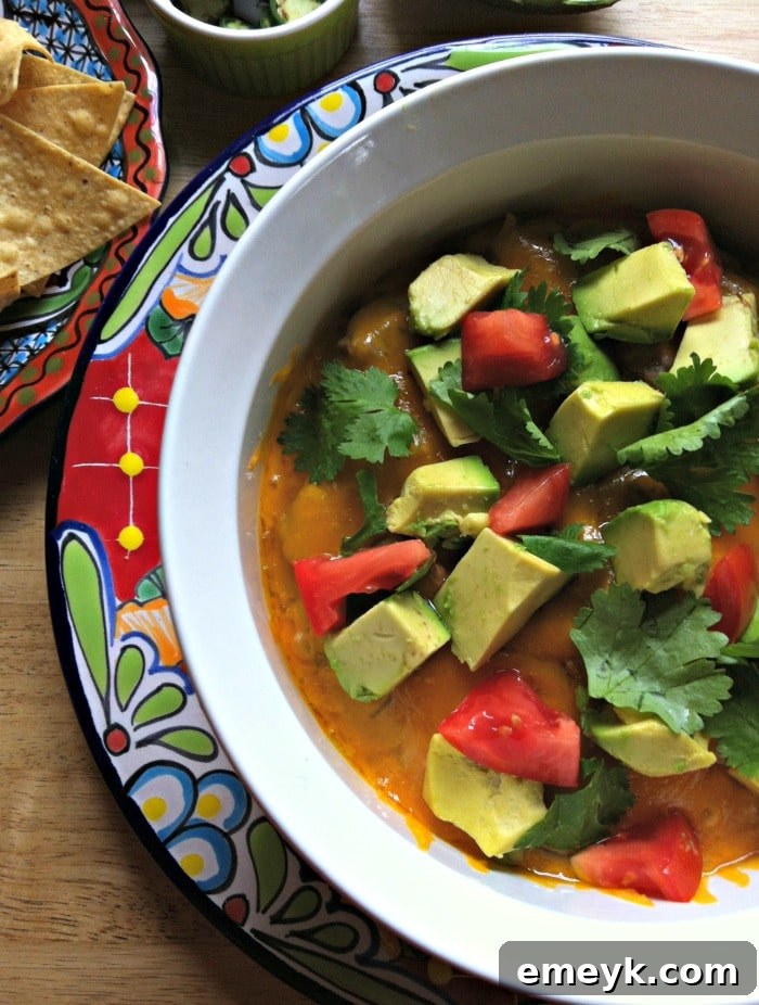Close-up shot of baked avocado black bean dip, showing bubbly cheese, fresh avocado slices, cilantro, and jalapenos