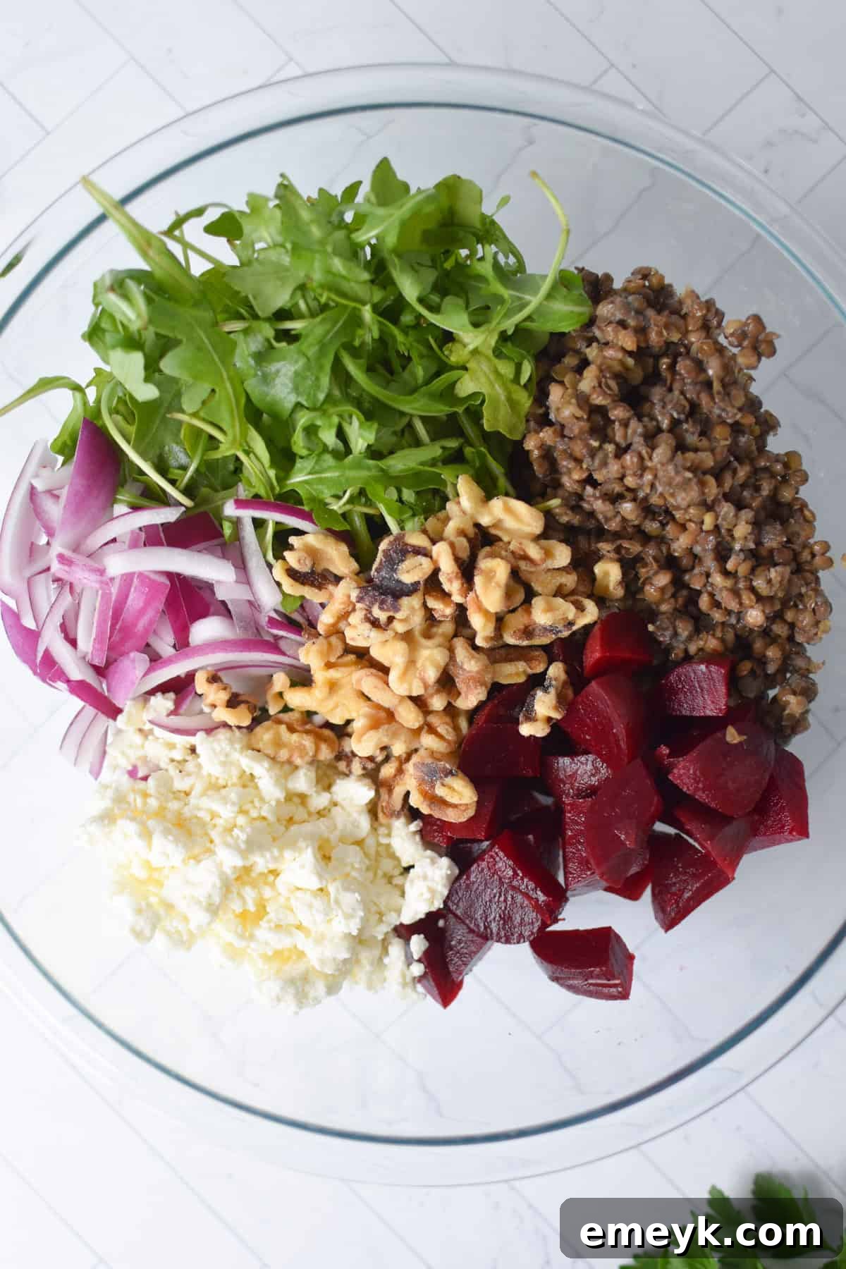 A clear glass bowl filled with the vibrant ingredients of Lentil Salad with Walnuts and Feta, ready to be tossed.