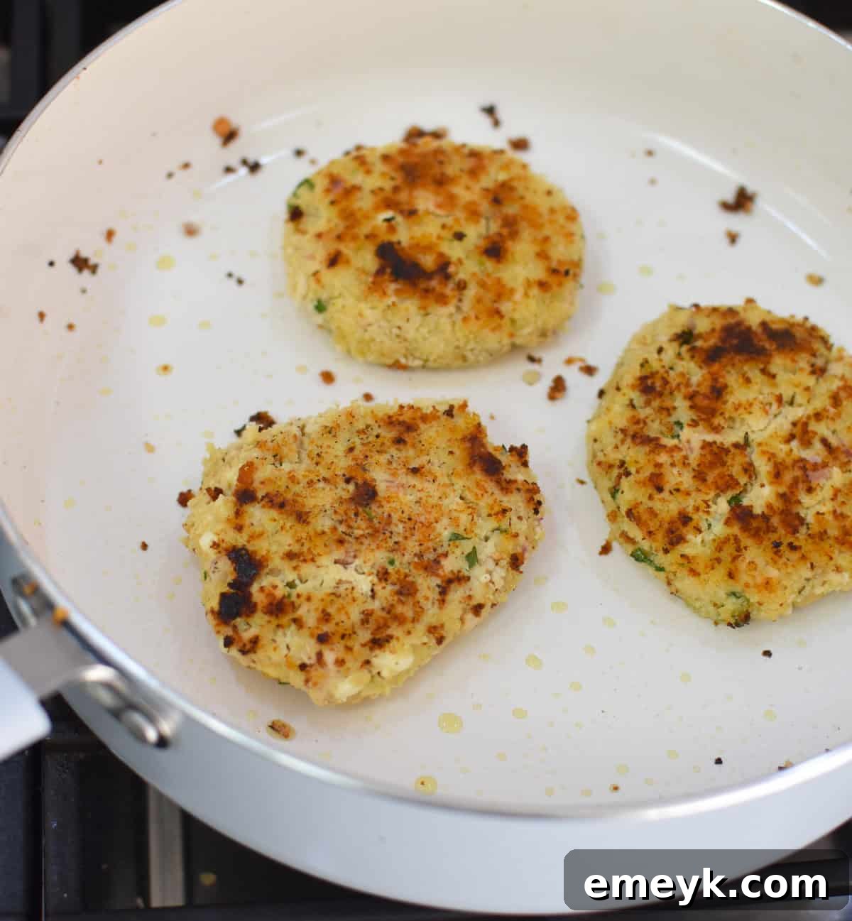 Mediterranean Salmon Cakes recipe cooking in a skillet, sizzling and turning golden