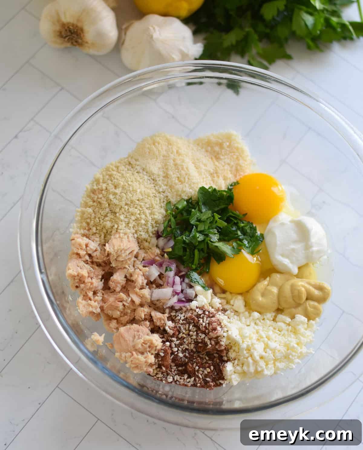Salmon Cakes Recipe Ingredients in a clear bowl, showing flaked salmon and fresh herbs