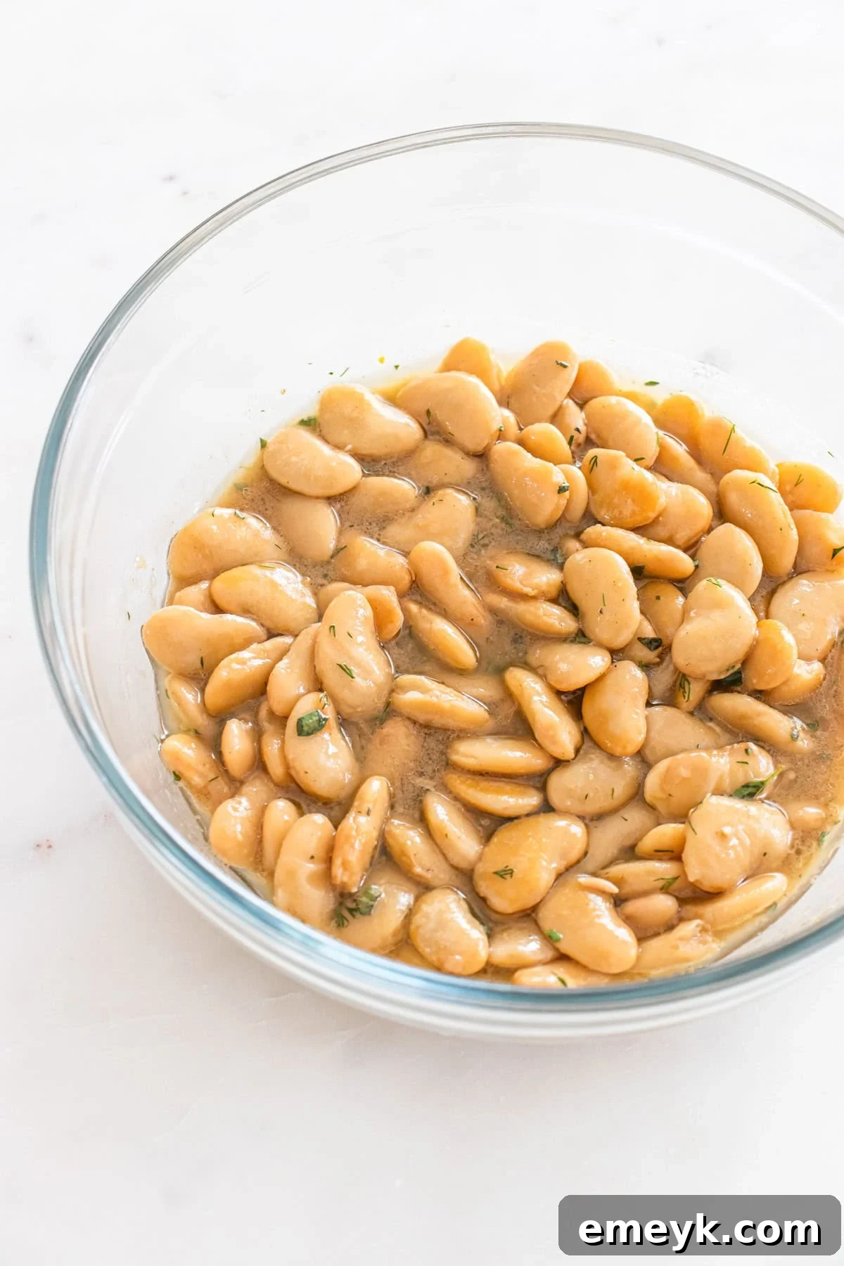 Drained butter beans being added to the prepared salad dressing.