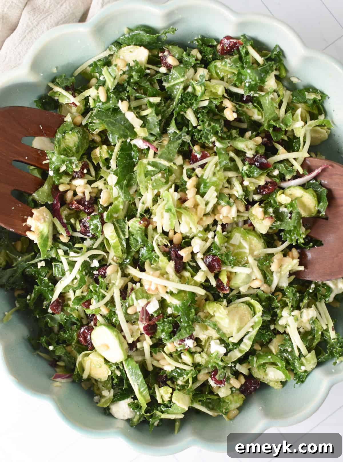 A large bowl of Kale Brussels Sprout Salad with wooden serving spoons, showcasing its vibrant colors and fresh ingredients.