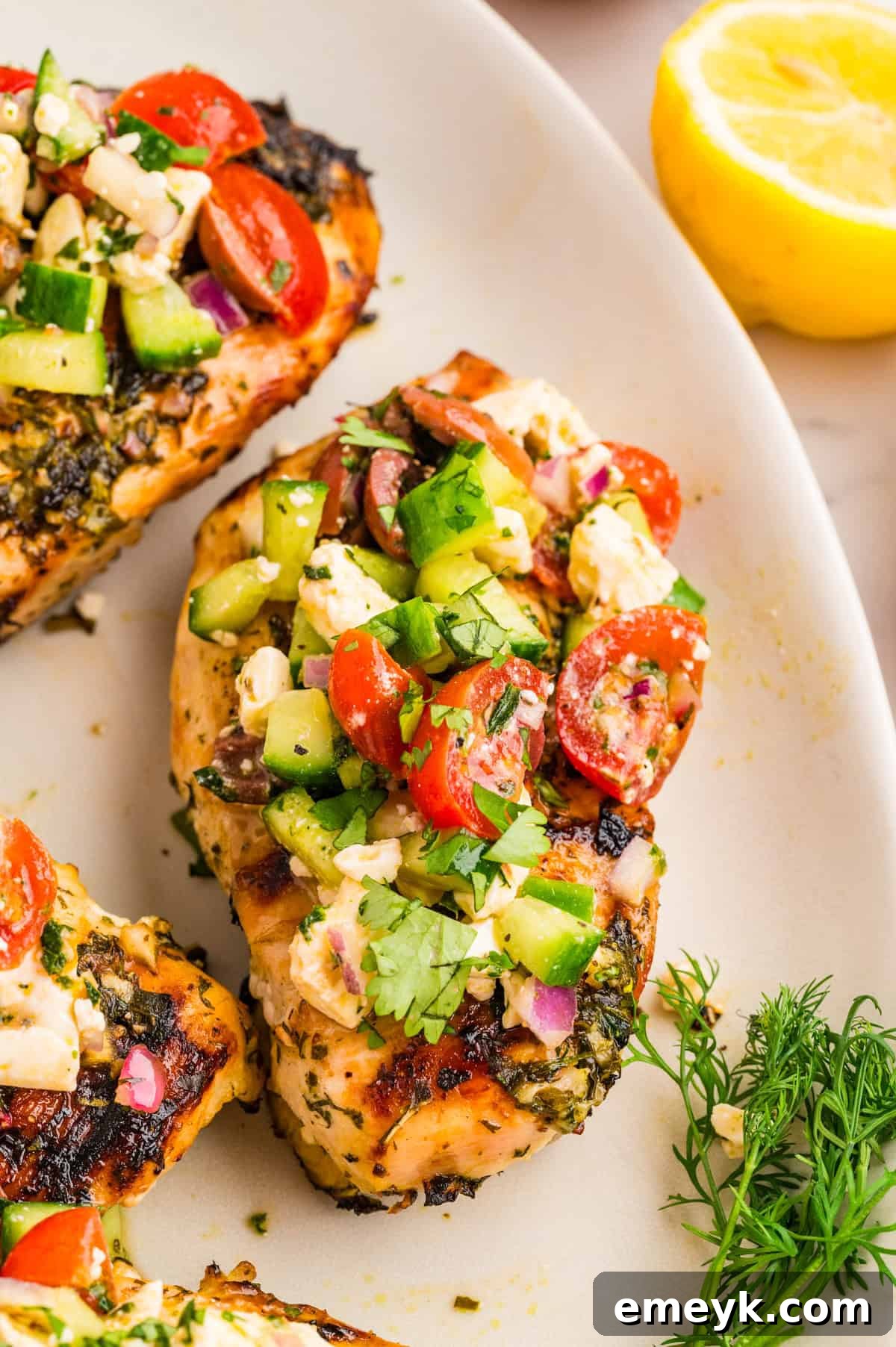 Grilled Mediterranean chicken breast topped with cucumber tomato olive and feta salad on a white plate