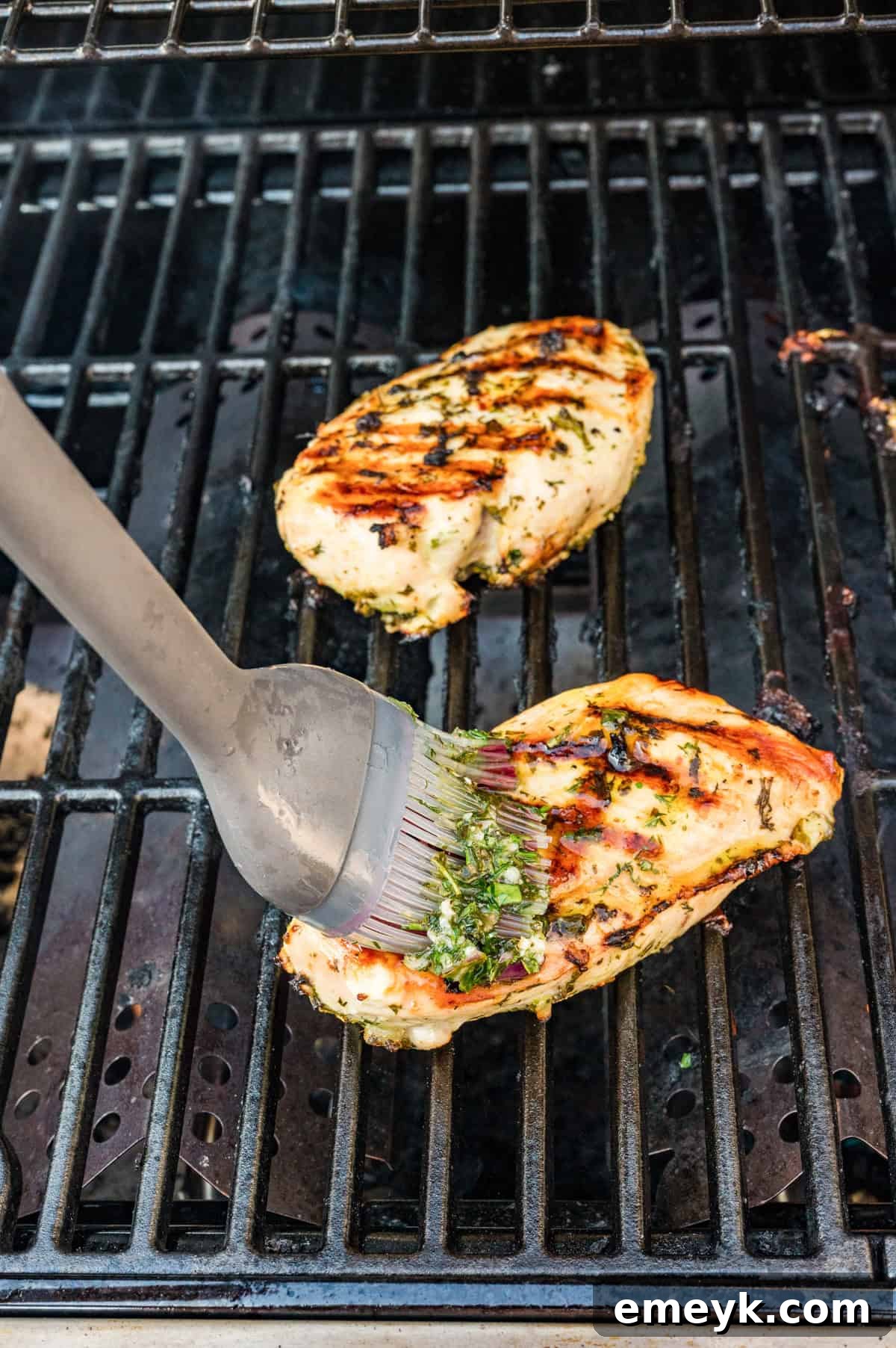 Marinated Mediterranean chicken breasts grilling with golden char marks on outdoor grill grates