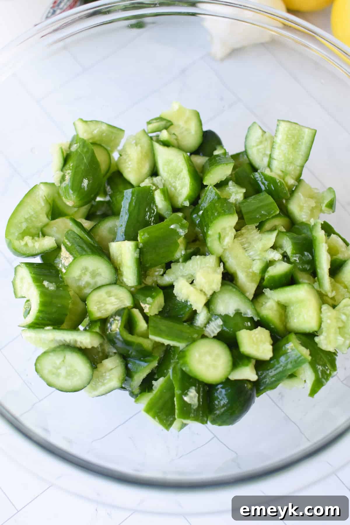 Smashed cucumbers in a glass bowl with salt, preparing to drain excess water.
