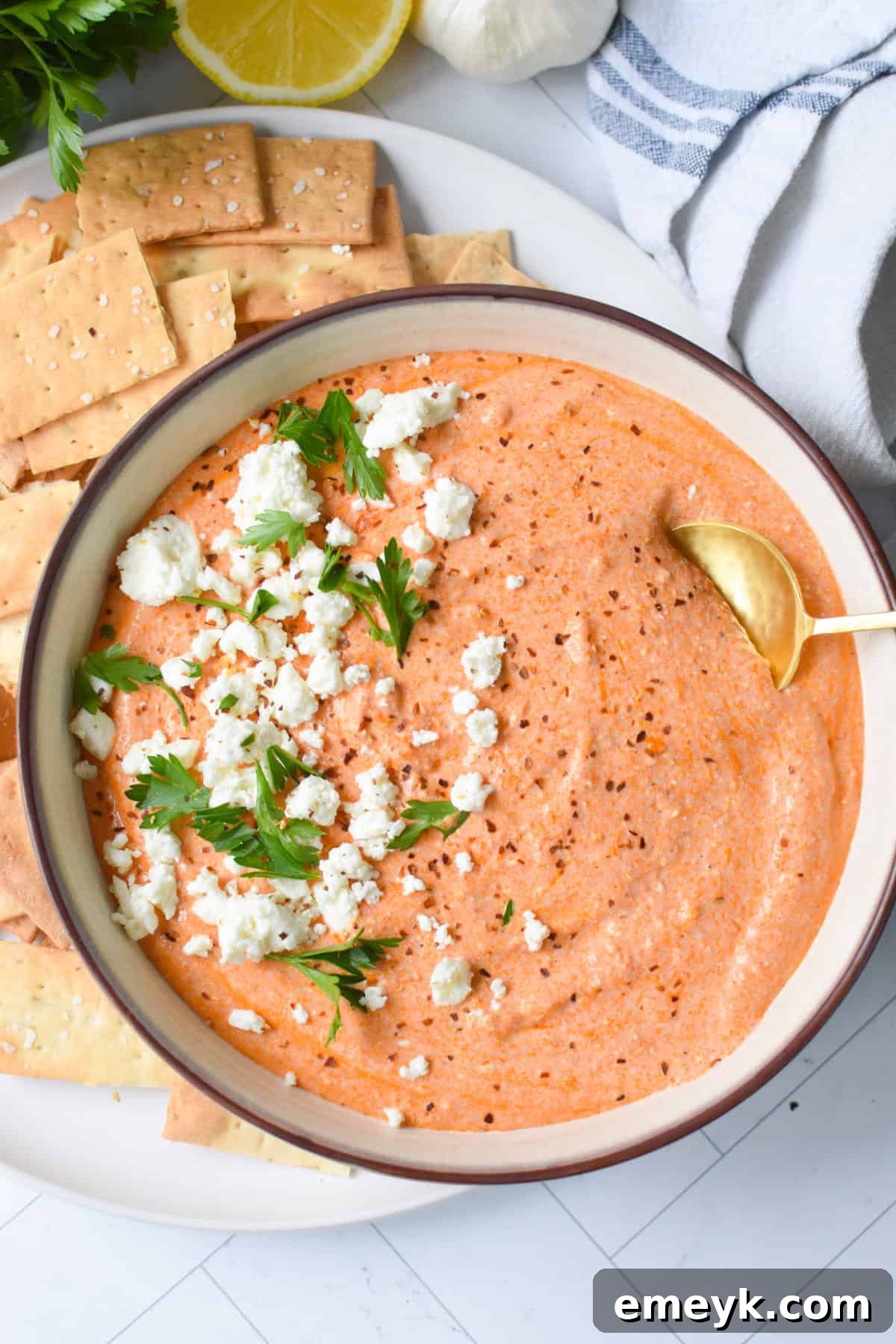 A bowl of creamy roasted red pepper and feta dip, garnished with parsley and feta crumbles, served with pita bread.