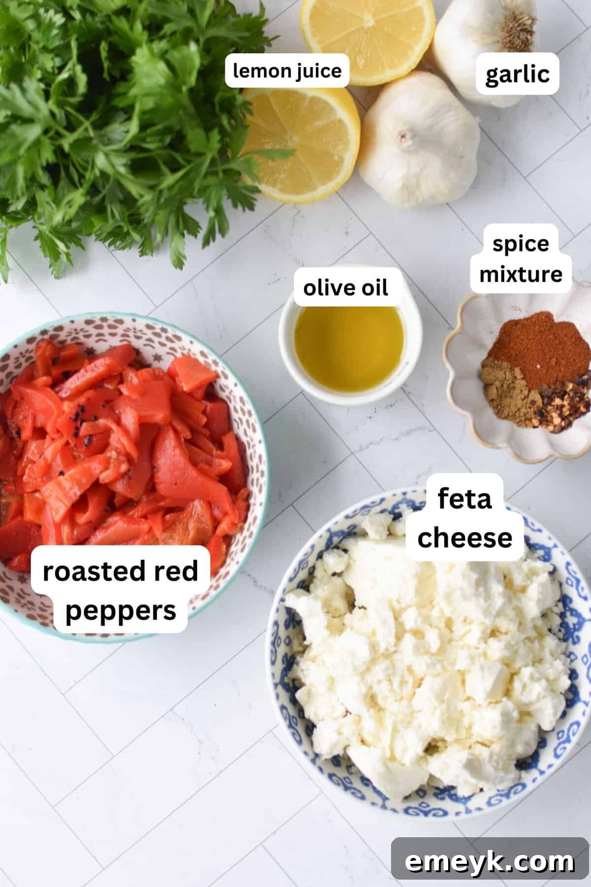 Ingredients for roasted red pepper feta dip laid out, including roasted peppers, a block of feta, garlic, lemon, and spices.