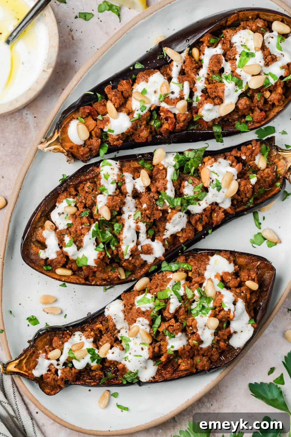 Mediterranean stuffed eggplant with ground beef and garlic yogurt sauce on a white serving dish