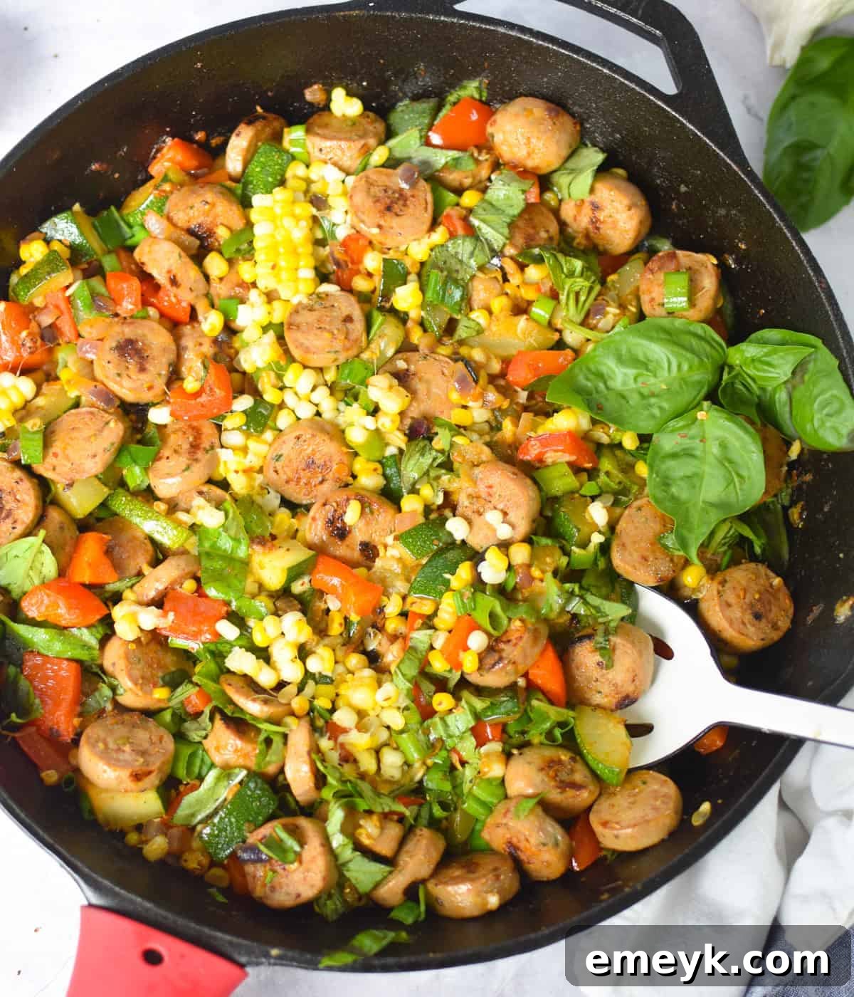Overhead shot of one-pan sausage and veggie skillet with fresh basil on top