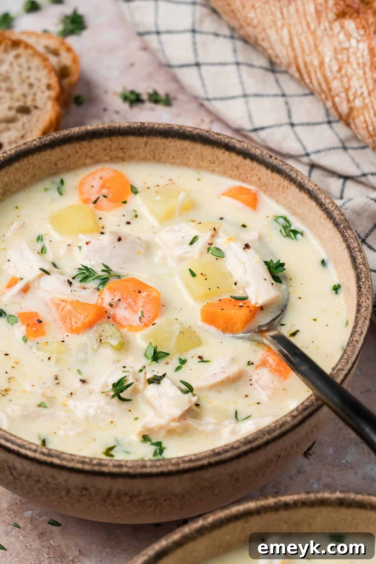 Bowl of creamy chicken potato soup topped with fresh thyme and cracked black pepper