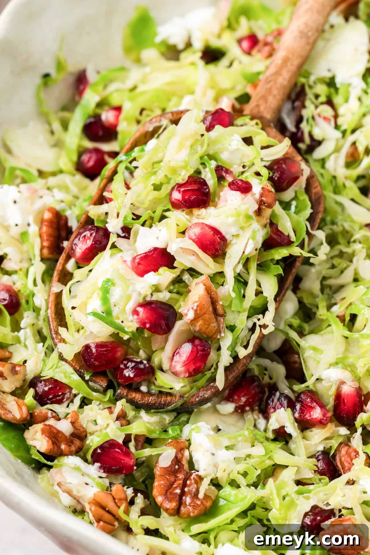 Brussels Sprout Salad in a white bowl with a wooden spoon